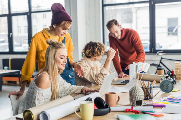 group of female and male designers working on startup project with laptops and blueprints in loft office