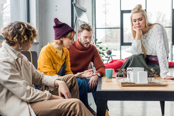 concentrated group of female and male architects sitting at table and working on house model in loft office