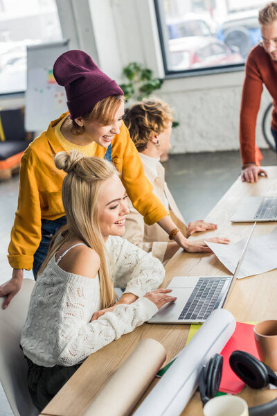 selective focus of group of female and male designers working on startup project with laptops and blueprints in loft office