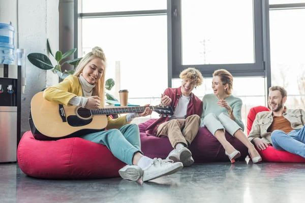 Happy Group Friends Sitting Bean Bag Chairs Playing Guitar — Stock Photo, Image