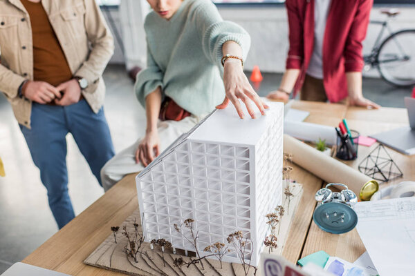 обрезанный вид группы женских и мужских архитекторов, работающих вместе над моделью дома в лофт-офисе
