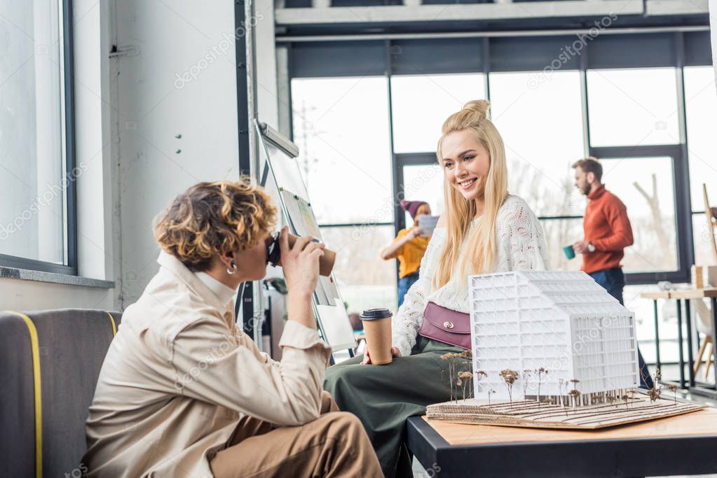 female and male architects with coffee to go looking at each other while working on house model in loft office