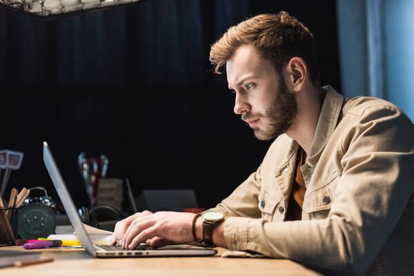 handsome casual businessman sitting at table and using laptop in office with copy space