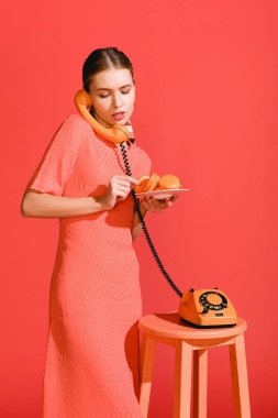 beautiful woman with macaroons and vintage rotary phone isolated on living coral. Pantone color of the year 2019 concept clipart