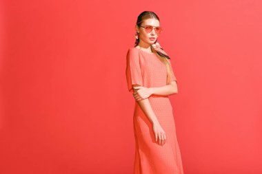 moda kız yaşayan poz mercan elbise ve kırmızı bir arka plan üzerinde güneş gözlüğü
