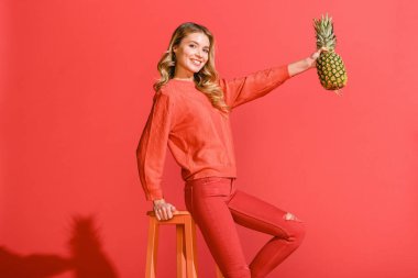 yaşam mercan izole dışkı, taze ananas tutan şık gülümseyen kadın 