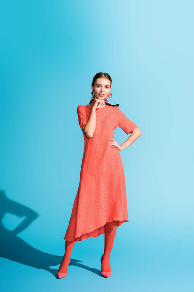 fashion shoot of stylish girl in trendy living coral dress posing on blue