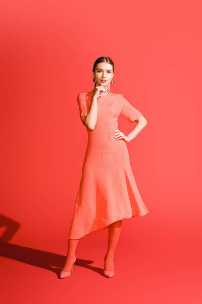 stylish young woman posing in living coral dress on red background