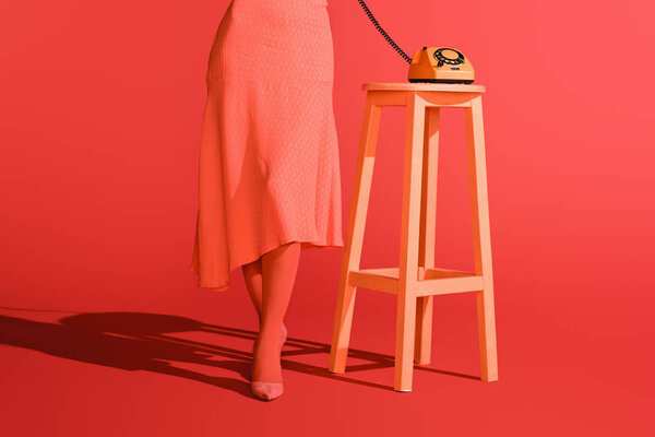 low section view of woman with retro rotary telephone on stool on living coral. Pantone color of the year 2019 concept
