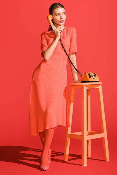 beautiful woman posing with retro rotary telephone on living coral. Pantone color of the year 2019 concept