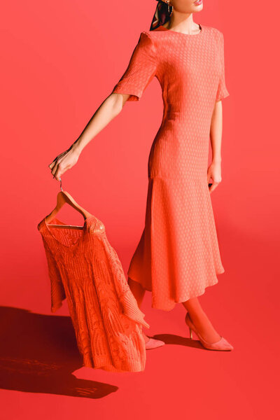 cropped view of stylish model holding hanger with clothing on living coral. Pantone color of the year 2019 concept