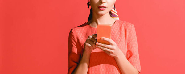 обрезанный вид девушки в живом коралловом платье с помощью смартфона на красном. Цвет пантона в концепции 2019 года

