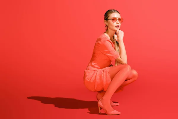 时尚模特摆在活珊瑚服装和太阳镜在红色背景 — 图库照片