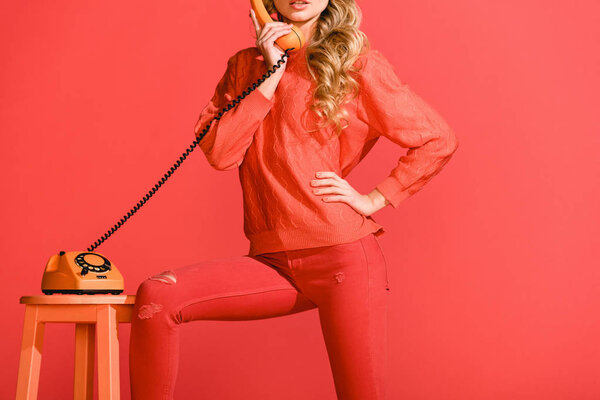 cropped view of girl posing with retro rotary telephone isolated on living coral. Pantone color of the year 2019 concept