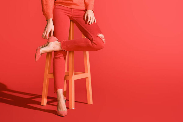cropped view of stylish girl posing in living coral clothing on stool on red background