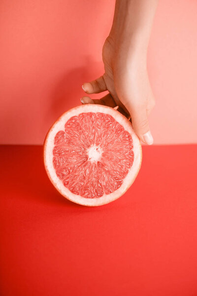 cropped view of female hand with grapefruit on living coral. Pantone color of the year 2019 concept