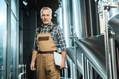 profesyonel üst düzey brewer not defteri tutan ve bira fabrikasında poz iş yarı tulumlar içinde