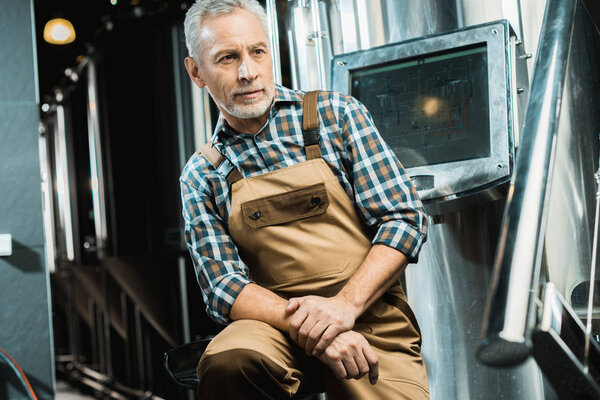 старший пивовар в комбинезоне, сидящий на пивоваренном заводе
