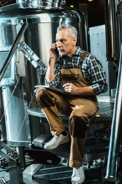 Cervecero Profesional Serio Overoles Trabajo Hablando Teléfono Inteligente Mientras Escribe — Foto de Stock