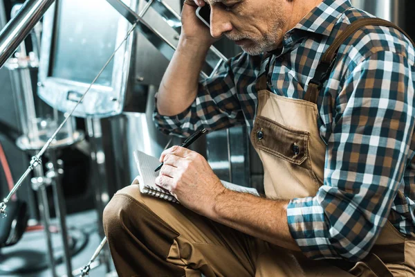 Senior Brewer Working Overalls Talking Smartphone While Writing Notepad Brewery — Stock Photo, Image