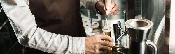 在啤酒厂的烧瓶里检查啤酒的酿酒师的裁剪视图 — 图库照片