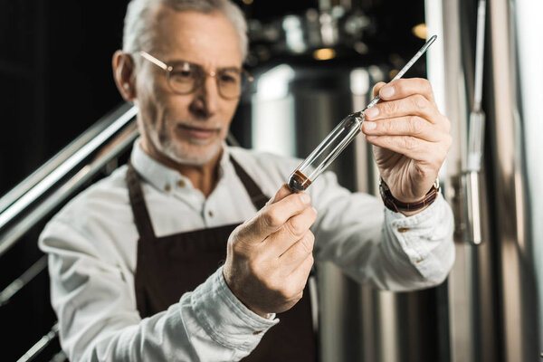 selective focus of male brewer examining beer in flask in brewery