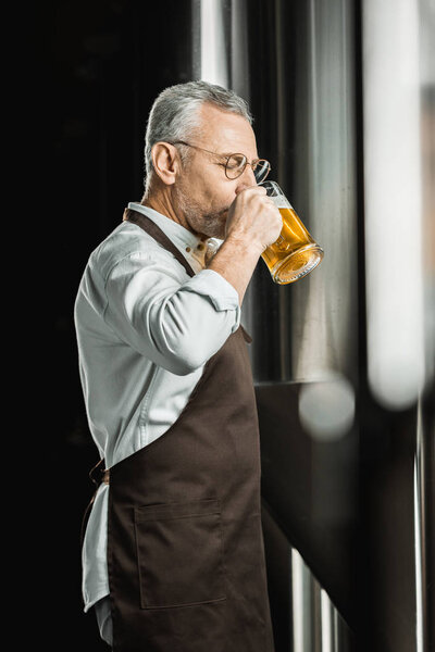 handsome male brewer drinking beer from glass in brewery