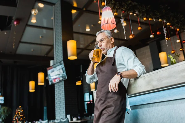バーのカウンターでビールを飲みを保持しているエプロンの男性労働者 — ストック写真