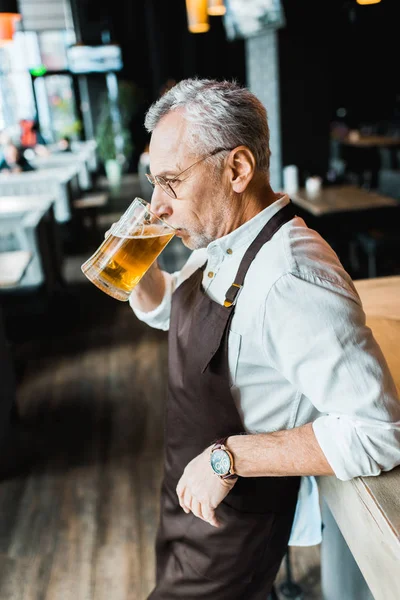 バーカウンターでビールを飲みを保持しているエプロンの先輩 — ストック写真