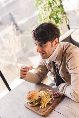neşeli adam patates kızartması lezzetli burger yakınındaki kafede kesme tahtası üzerinde tutan