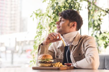 patates kızartması lezzetli burger yakınındaki kafede kesme tahtası üzerinde tutarak neşeli genç adam