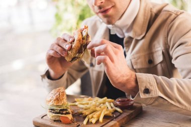 lezzetli burger patates kızartması yakınındaki kafede kesme tahtası üzerinde tutan genç adam görünümünü kırpılmış