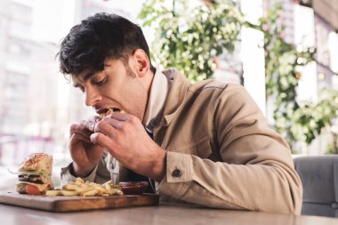 genç adamın lezzetli hamburger patates kızartması yakınındaki kafede kesme tahtası üzerinde yemek seçici odak