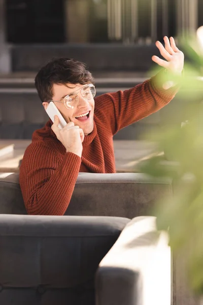 Smiling Young Man Glasses Talking Smartphone While Waving Hand Cafe — Stock Photo, Image