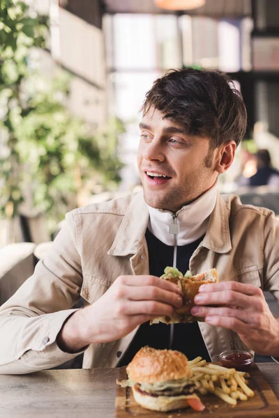 Enfoque Selectivo Sonriente Joven Sosteniendo Sabrosa Hamburguesa Cerca Papas Fritas — Foto de Stock