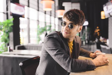 mutlu genç adam, sayaç Kupası yakınındaki bar kahve ile oturmak güneş gözlüğü