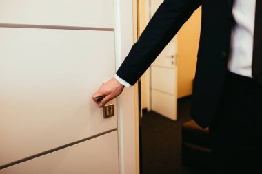 partial view of man holding door handle and coming into hotel room clipart