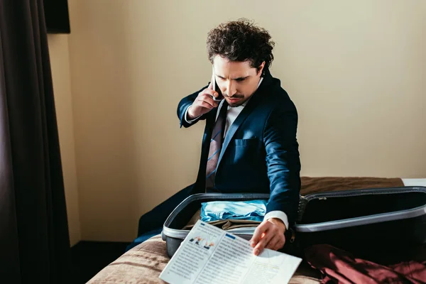 Businessman Talking Smartphone Holding Newspaper While Sitting Bed Suitcase Hotel — Stock Photo, Image