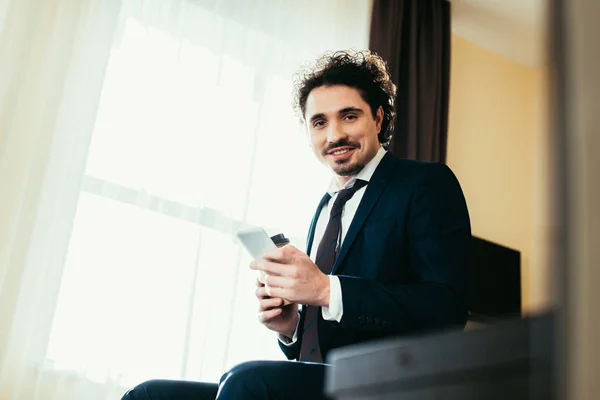 在酒店房间出差时使用智能手机的微笑的商人 — 图库照片