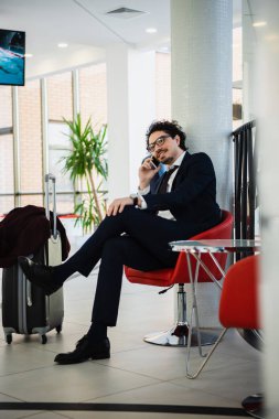 seyahat çantası ile otel lobisinde beklerken smartphone cep telefonu ile konuşurken gülümseyen iş adamı