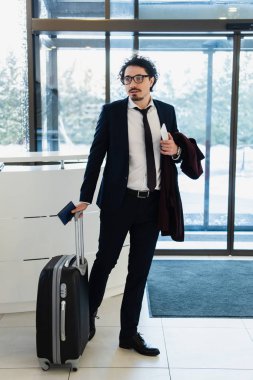 Otelin Resepsiyon masasında duran smartphone, pasaport ve seyahat çantası ile işadamı