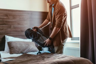 erkek turist otel odasında yatağın yanında sırt çantası elinde görünümünü kırpılmış