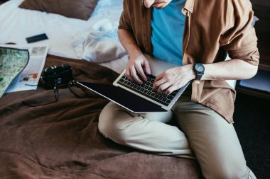 kırpılmış gazete, harita ve fotoğraf kamera yatakta ile otel odasında dizüstü kullanarak Gezgin görünümünü