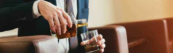 cropped view of businessman pouring whiskey from bottle into glass in hotel room 