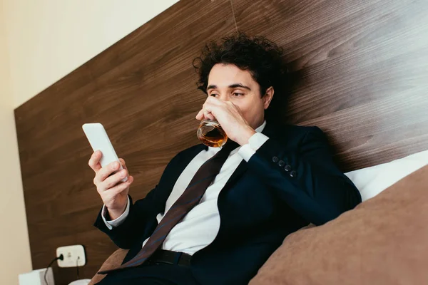 Ενηλίκων Επιχειρηματίας Χρησιμοποιώντας Smartphone Και Πίνει Ουίσκι Κρεβάτι Δωμάτιο Ξενοδοχείου — Φωτογραφία Αρχείου