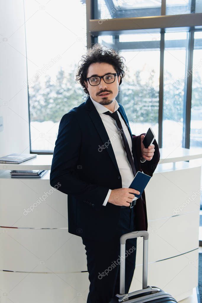 businessman with smartphone, passport and baggage waiting for check-in at the hotel