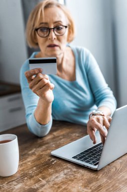kredi kartı tutan ve evde online alışveriş yaparken dizüstü kullanarak kadın kıdemli