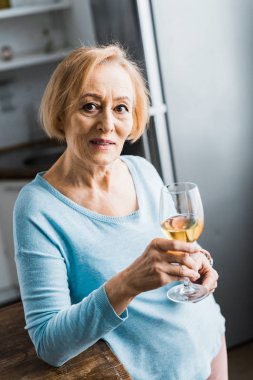 Kameraya bakarak ve evde şarap bardağını tutan kadın kıdemli seçici odak