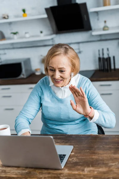 Sonriente Mujer Mayor Sentada Mesa Saludando Con Mano Mientras Tiene —  Fotos de Stock