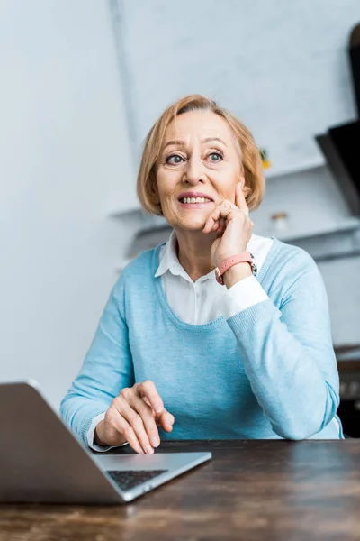 Uśmiechnięta Zamyślony Starszy Kobieta Siedzi Przy Stole Laptopa Wspierają Podbródek — Zdjęcie stockowe